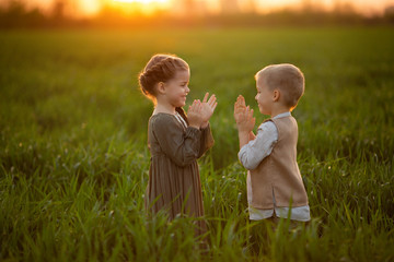 Two cheerful twin children, a girl and a boy in rustic clothes, play and have fun at sunset in a...