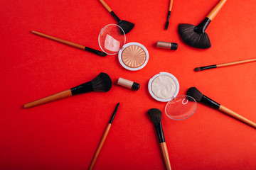 Cosmetics on a bright orange background. Makeup brushes, highlighter and eye shadow with pigments