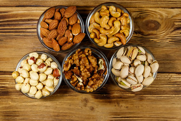 Assortment of nuts on wooden table. Almond, hazelnut, pistachio, walnut and cashew in glass bowls. Top view. Healthy eating concept