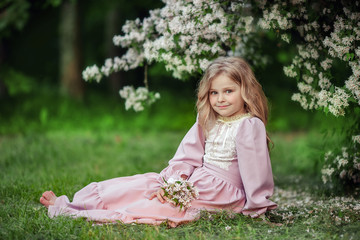 Spring portrait of a beautiful cute girl in a pink dress in a flowered garden.
