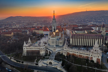 Fototapeta na wymiar Budapest, Hungary - Aerial view of the famous Fisherman's Bastion (Halaszbastya) and Matthias Chruch at sunset with the sun right behind the church tower. Gold and blue sky at winter time