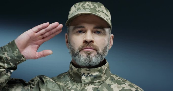 Close up of the Caucasian US soldier in the uniform and hat, ith gray beard saluting and putting hand to head gesture. Portrait.