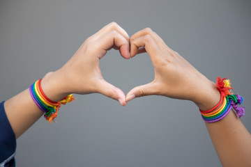 hand of LGBT women holding together, forming heart shape with rainbow ribbon symbol; concept of...