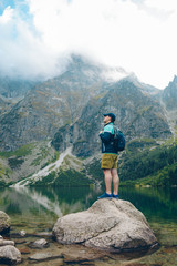 man with backpack looking at lake in mountains