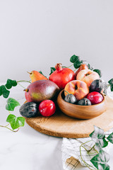 Fototapeta na wymiar Assorted fruits in a wooden plate on a marble background, green ivy mango, peach, plum, pear, pomegranate, fig peach
