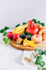 Assorted fruits in a wooden board on a marble background, green ivy mango, peach, plum, pear, pomegranate, fig peach