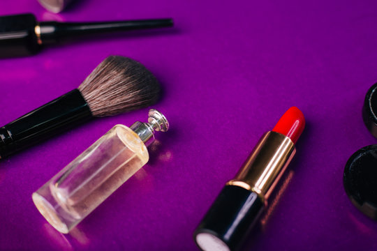 Scattered cosmetics on a purple background. The contents of women's handbags. Lady set. Lipstick, perfume and shadow. View from above - Powered by Adobe