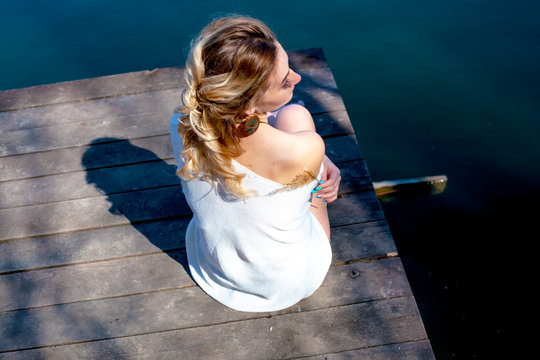 Rear view of the back of woman relax in the wood piar near the lake. Female hands hug herself and look to wildlife of the nature. model wearin bohemian accessories and oversize sweater.