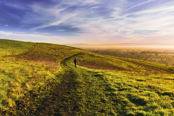 Sunset view of hiker walking on a trail on the verdant hills of East San Francisco Bay Area;...