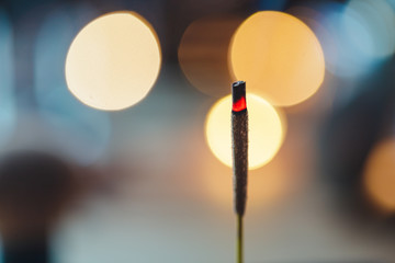 Incense stick burns against blurred candle lights. Macro photography.