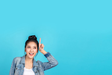 Happy asian woman feeling happiness and standing pointing hands up to copyspace on blue background.Cute asia girl smiling wearing casual jeans shirt and finger pointing to above for present promotions © ChayTee