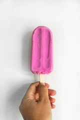 woman hand holding pink stick ice scream for summer refreshment on white concrete wall background