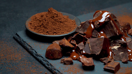 Grated brown chocolate on a plate, next to large pieces of chocolate and melted poured on top