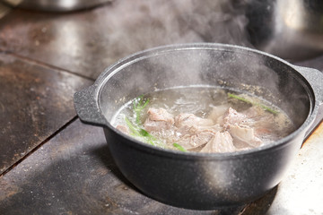Traditional beef broth with vegetable, bones and ingredients in pot, cooking recipe. Soup in a cooking pot with ladle on dark stone background. Top view