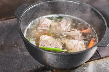 Traditional beef broth with vegetable, bones and ingredients in pot, cooking recipe. Soup in a cooking pot with ladle on dark stone background. Top view