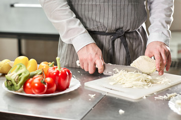 Closeup of hand with knife cutting fresh vegetable. Young chef cutting beet on a white cutting board closeup. Cooking in a restaurant kitchen
