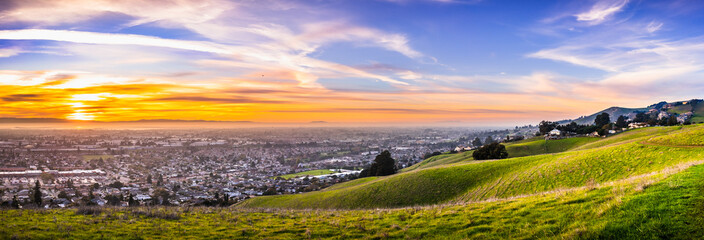 Sunset view of residential and industrial areas in East San Francisco Bay Area; green hills visible...