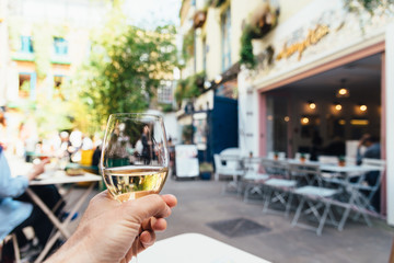 Man holds a glass of white wine in a trendy shopping area sitting on a terrace