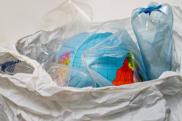 The globe is in a bag with plastic trash. A model of the planet Earth was thrown into the trash can along with empty bottles and glasses. The concept of environmental pollution by plastic waste. .