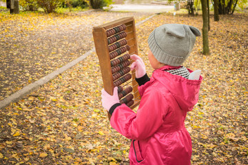 Little girl scores on old mechanical abacus in the autumn park. A child learns to count numbers on...