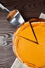 Pumpkin pie on cutting board on brown wooden table, top view. Piece of Thanksgiving pie on cake spatula