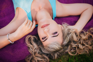 Obraz na płótnie Canvas Beautiful girl on a picnic in the park. Blonde lying on a purple bedspread resting. Model with a cheerful smile