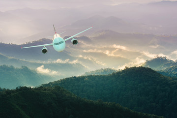 Fototapeta premium Airplane is flying over mountains in fog at sunset in winter. Landscape with passenger airplane, Business travel,Commercial plane,Aerial view.