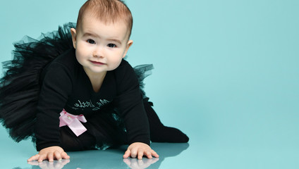 Little kid in black bodysuit with pink bow, poofy skirt and socks. She smiling, sitting on blue background. Close up, copy space