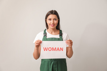 Female worker holding paper with text WOMAN on light background. Concept of feminism