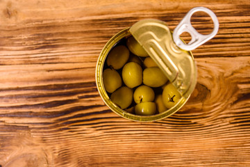 Opened tin can with green olives on wooden table. Top view