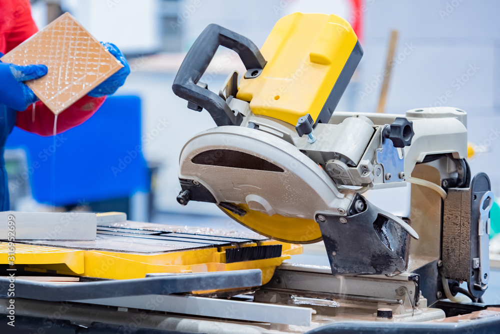 Poster master is next to the circular saw. tile processing. man holds a cut tile in his hands. man works wi