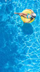 Active young girl in hat in swimming pool aerial top view from above, child relaxes and swims on inflatable ring donut and has fun in water on family vacation, tropical holiday resort