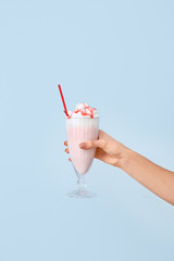 Female hand with glass of tasty milkshake on color background