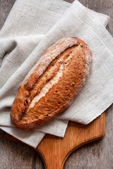 Loaf of whole wheat bread wooden board on kitchen table. Flat lay, top view
