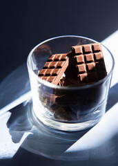 Chocolate bars in a glass vase in the sunlight rays cast shadow.