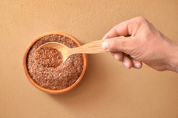 Male hand with spoon of flax seeds on color background