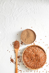 Bowls with flax seeds, powder and spoon on white background