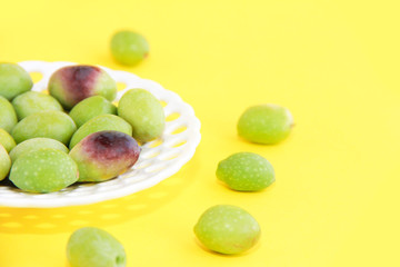 natural fresh green and burgundy olives in a white decorative plate on a yellow background