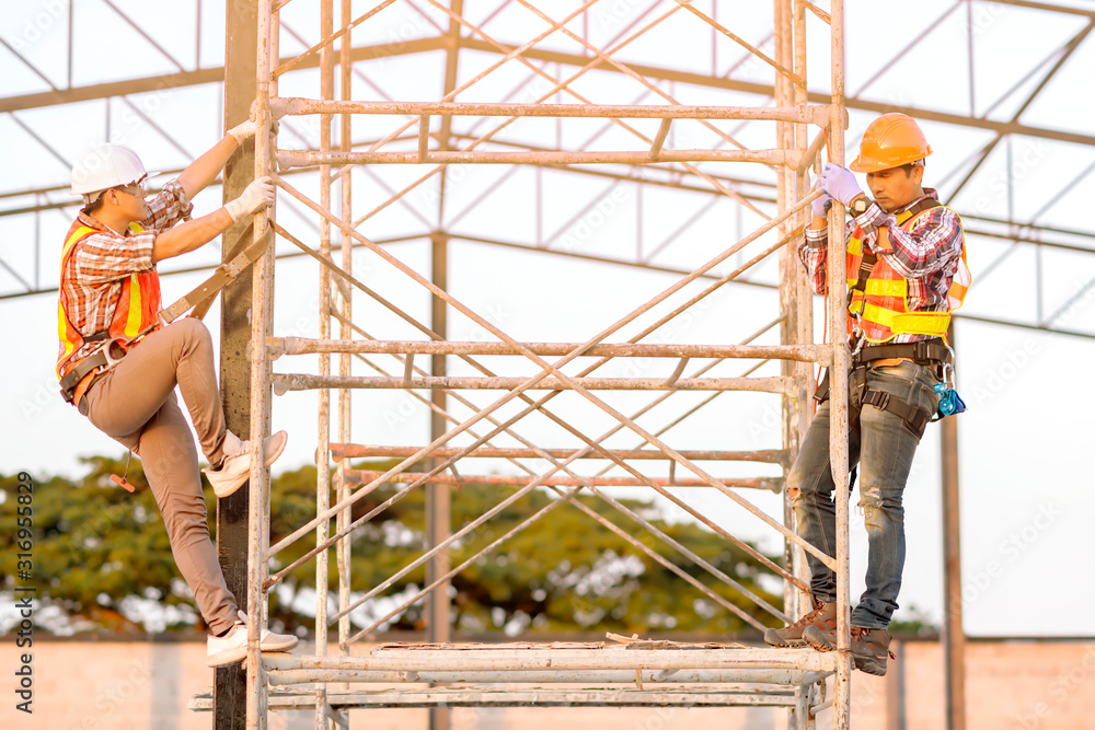 Poster technicians in safety clothing are climbing scaffolding. friends go up and check the strength of the