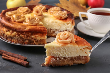 Cheesecake with apples decorated with roses from apples located on a dark background and cup of tea, Horizontal orientation