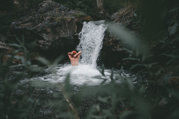 young red-haired girl bathes in a cold mountain waterfall in a green coniferous forest