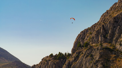 Paraglider flies towards the steep slopes of the mountains against the blue sky, Omis, Croatia