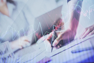 A woman hands writing information about stock market in notepad. Forex chart holograms in front. Concept of research. Double exposure