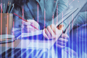 Fototapeta premium A woman hands writing information about stock market in notepad. Forex chart holograms in front. Concept of research. Multi exposure