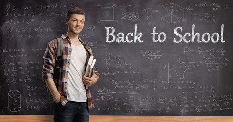 Male student with books standing in front of a blackboard with text back to school