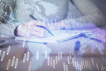 Hands writing information about stock market in notepad. Forex chart holograms in front. Concept of research. Multi exposure