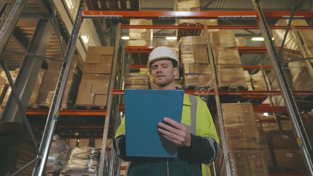 Low angle portrait of warehouse worker holding clipboard while doing stock inventory