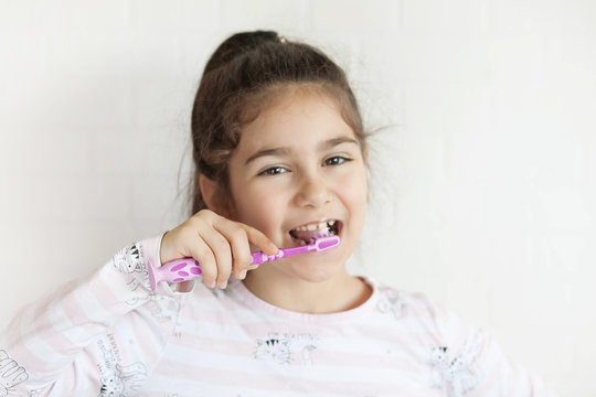 Happy cute little child girl brushing her teeth on light background. Space for text. Healthy teeth.