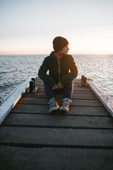 young traveling girl sits on a pier on the background of the sea and looks at the sunset - 316958247