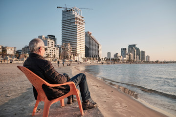 senior old man sitting in a chair realxing in the beach in Tel Aviv - ISRAEL. - obrazy, fototapety, plakaty